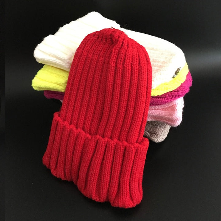 Rote Strickmütze aus Wolle, gestapelt auf bunte Mützen, Wintermode Accessoire, unisex.
