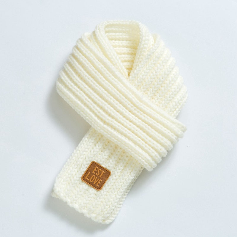 Weiße gestrickte Schal aus Wolle mit braunem Lederetikett, modisches Winteraccessoire.