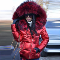 Frau in roter Daunenjacke mit Kunstfellkapuze, Sonnenbrille, Wintermode, draußen.