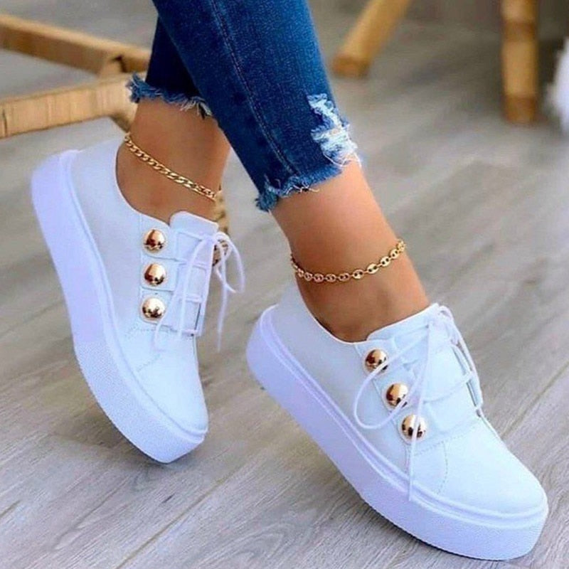 Weiße Damen-Sneaker mit goldenen Knöpfen, Jeans, Holzfußboden, modische Freizeitschuhe.