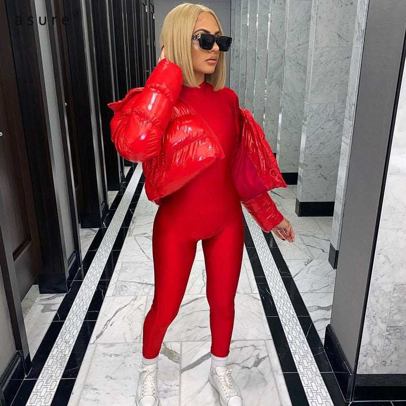 Frau in rotem Jumpsuit und roter Daunenjacke, blonde Haare, schwarze Sonnenbrille, weiße Sneaker.