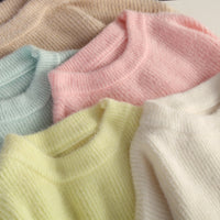 Fünf gestrickte Pullover in Pastellfarben: Beige, Blau, Rosa, Gelb, Weiß, aus weichem Material.