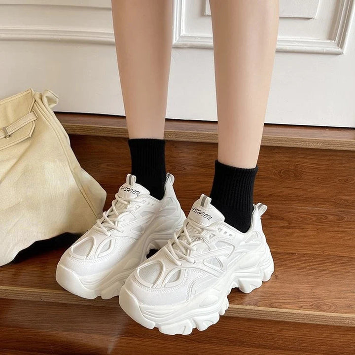 Weiße Damen-Sneaker, stilvoll und bequem, auf Holzboden mit schwarzem Socken.