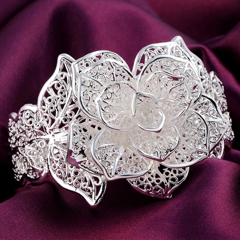 Silbernes filigranes Blumenarmband auf lila Stoff, eleganter Schmuck, Damenaccessoire.