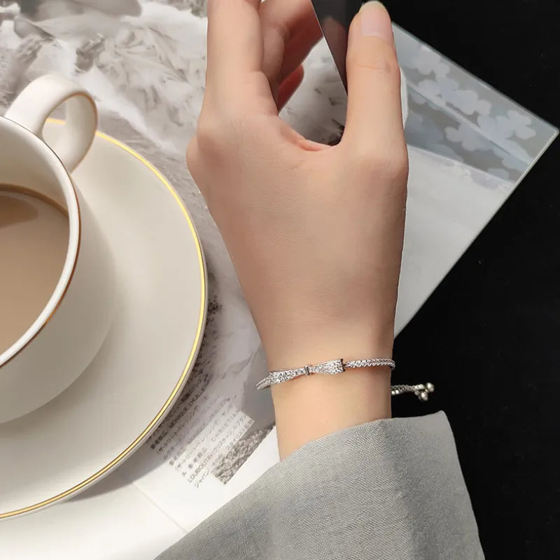 Silbernes Armband mit Strasssteinen an Hand, neben Kaffeetasse und Zeitschrift.