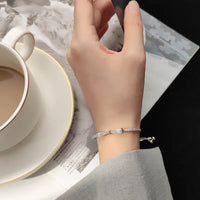 Silbernes Armband mit Strasssteinen an Hand, neben Kaffeetasse und Zeitschrift.