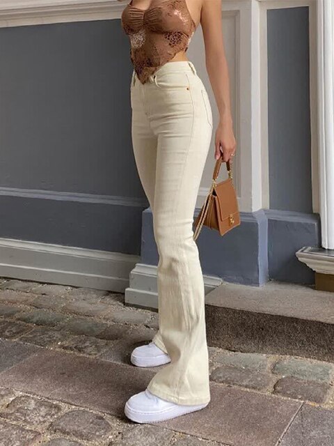 Frau in cremefarbener Schlaghose, Spitzenoberteil, braune Tasche, weiße Plateau-Sneaker.