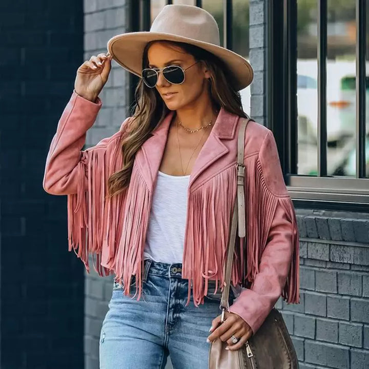 Frau in rosa Fransenjacke, Sonnenbrille und Hut, lässiger Streetstyle-Look.