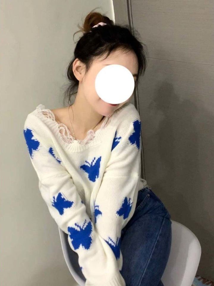 Frau in weißem Pullover mit blauen Schmetterlingen, sitzt auf Stuhl, lässige Mode.