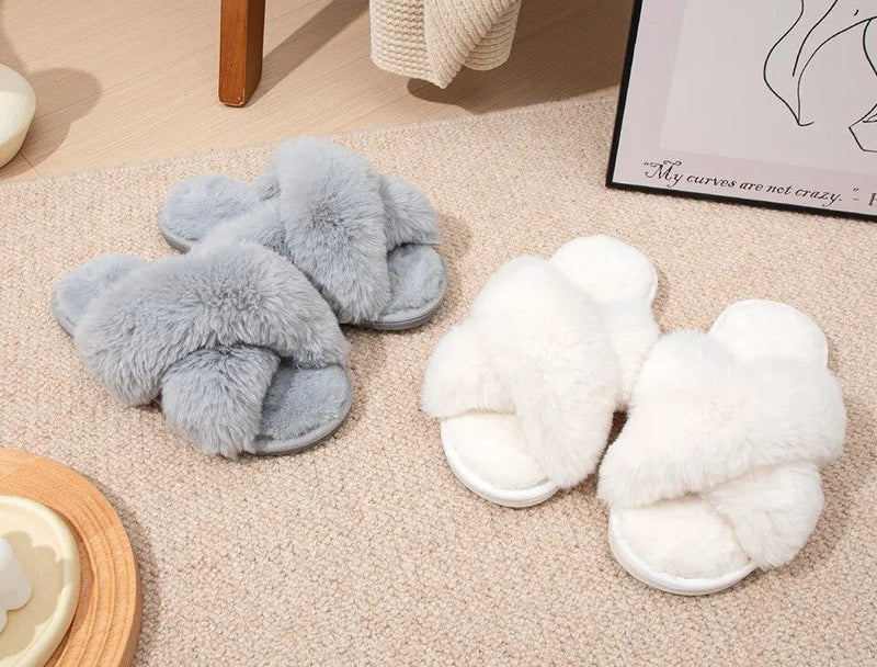 Graue und weiße flauschige Hausschuhe aus Kunstfell auf Teppichboden.