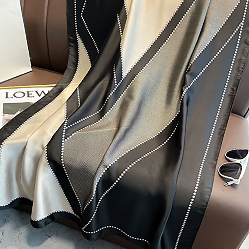 Schwarzer und beiger Seidenschal mit geometrischem Muster auf Ledersofa.