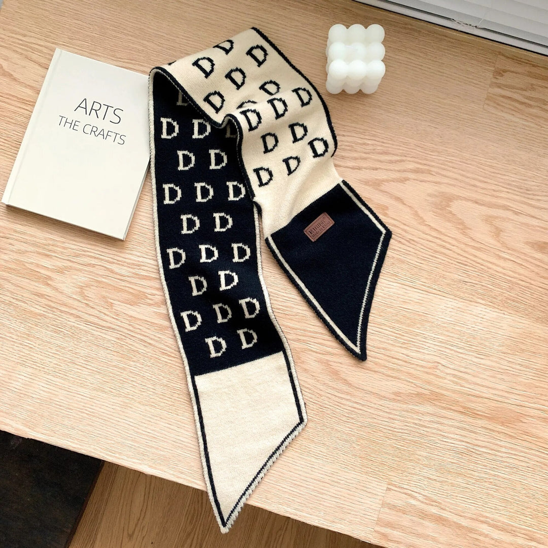 Schwarzer und beiger Designer-Schal mit D-Muster auf Holztisch neben Buch und Kerze.