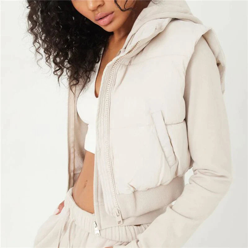 Frau in beiger Steppweste mit Kapuze, weißem Top und Jogginghose, Freizeitmode.