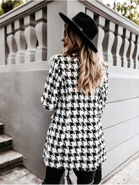 Frau im schwarz-weiß karierten Mantel und schwarzem Hut, stilvolle Herbstmode, Rückansicht.