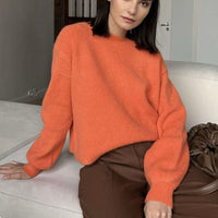 Frau in orangefarbenem Strickpullover, braune Hose, sitzt auf Sofa, modisch, gemütlich.