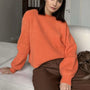 Frau in orangefarbenem Strickpullover, braune Hose, sitzt auf Sofa, modisch, gemütlich.
