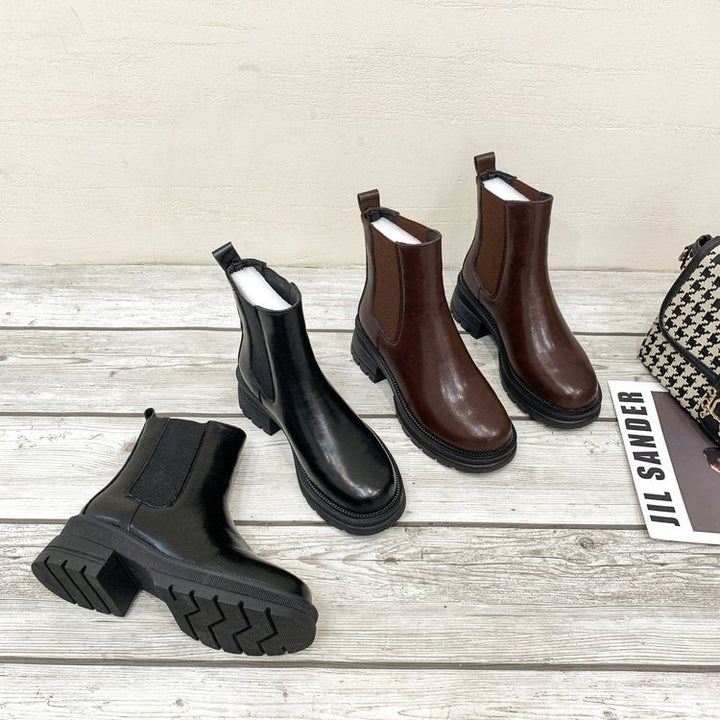 Schwarze und braune Chelsea Boots aus Leder mit Blockabsatz auf Holzboden.