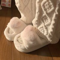 Weiße flauschige Hausschuhe auf Holzfußboden, gestrickte Socken, gemütliche Wintermode.