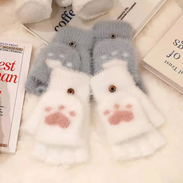 Flauschige weiße und graue Handschuhe mit Katzenpfoten-Design auf einem Tisch.