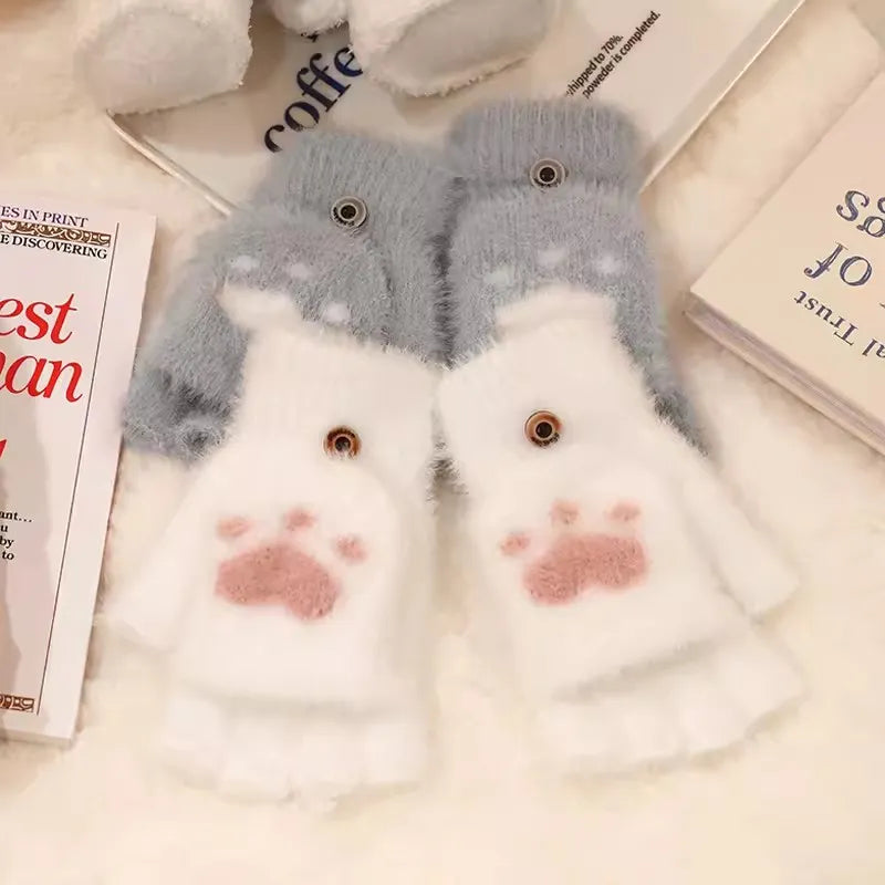 Flauschige weiße und graue Handschuhe mit Katzenpfoten-Design auf einem Tisch.