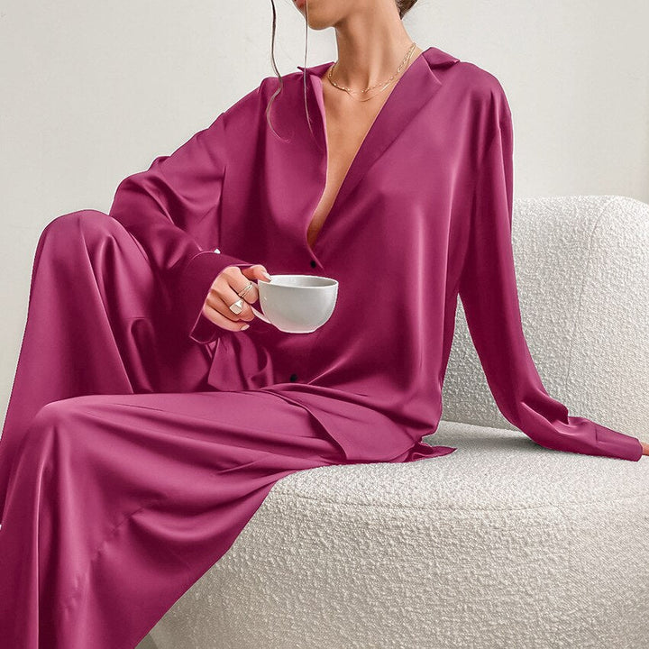 Frau in fuchsia Satin-Pyjama, sitzt auf weißem Sofa, hält eine Tasse, elegantes Nachtwäsche-Design.
