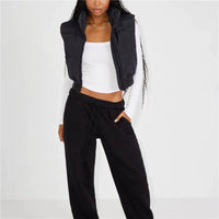 Frau in schwarzer Steppweste und Jogginghose, weißes Langarmshirt, modische Freizeitkleidung.