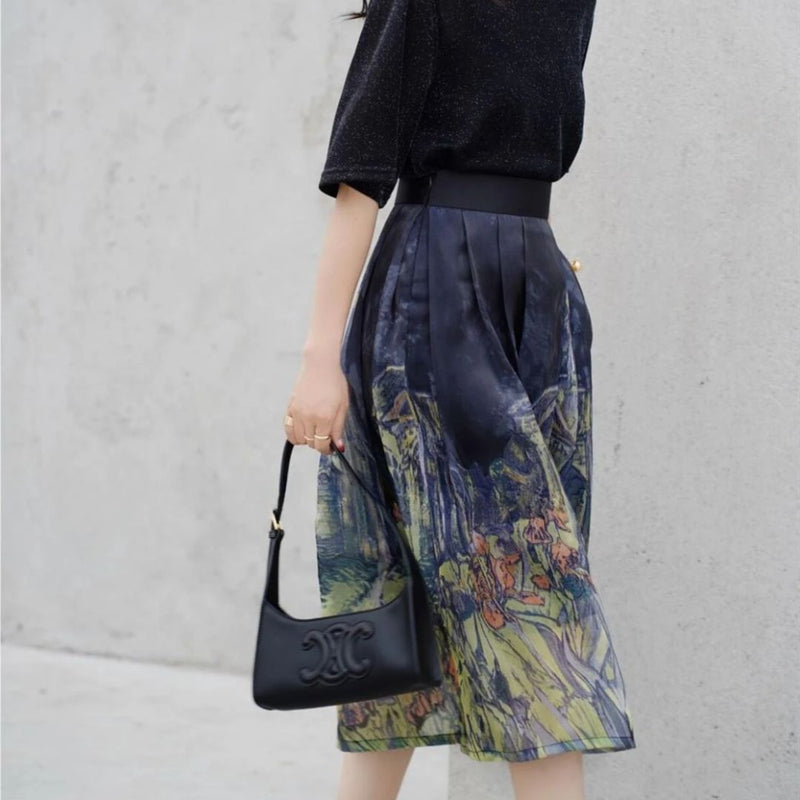 Frau in schwarzem Oberteil und bedrucktem Rock mit schwarzer Designer-Handtasche.