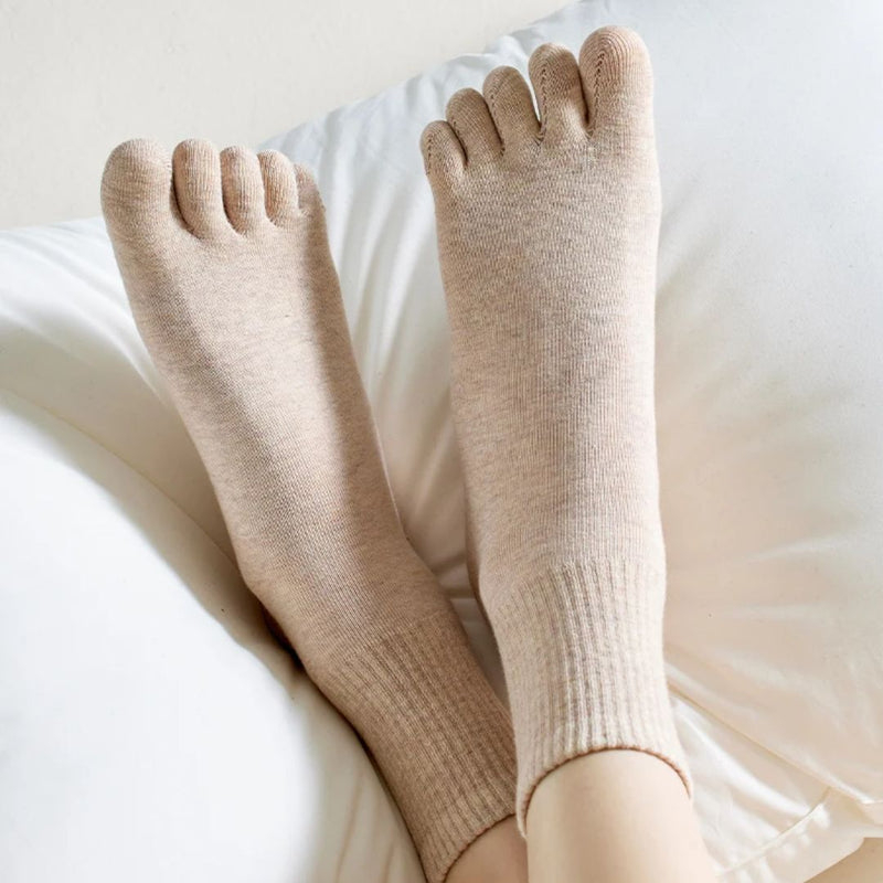 Beige Zehensocken aus Baumwolle auf weißem Kissen, bequem und atmungsaktiv für den Alltag.