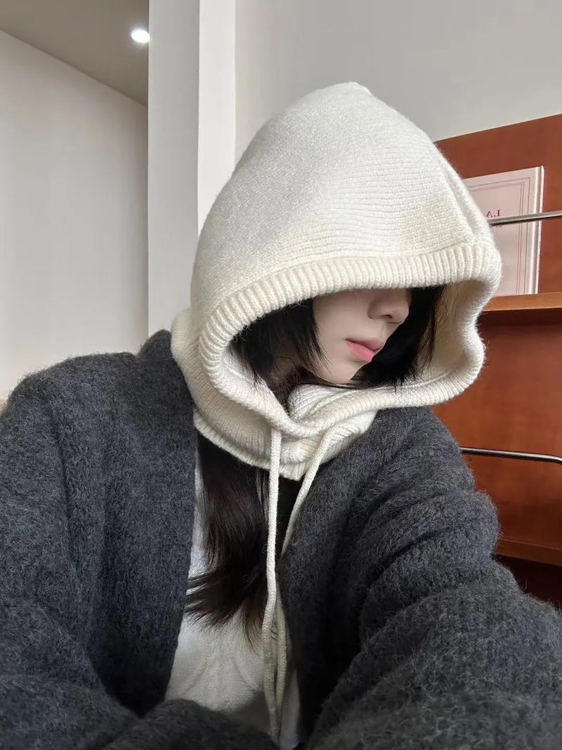 Frau mit beigem Strick-Hoodie und grauem Wollmantel in modernem Raum.