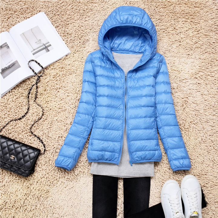 Blaue Daunenjacke mit Kapuze, Damenmode, leicht, warm, auf Teppich mit Tasche und Schuhen.