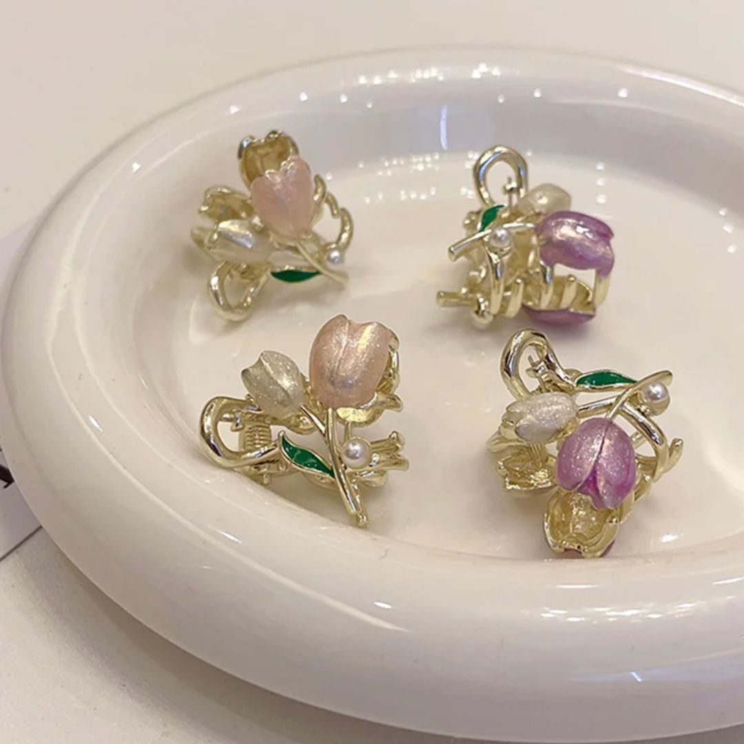 Goldene Blumenohrringe mit rosa und weißen Blüten, Perlenakzenten auf weißem Teller.