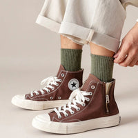 Braune High-Top-Sneaker mit Reißverschluss, grüne Socken, weiße Schnürsenkel, lässiger Stil.