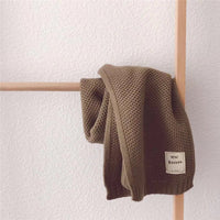 Braune Strickdecke aus Baumwolle auf Holzleiter, weiches Material, ideal für Wohnzimmer-Dekoration.