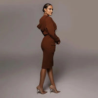 Frau in braunem Kapuzenkleid und transparenten High Heels, seitlich stehend.