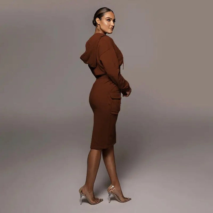 Frau in braunem Kapuzenkleid und transparenten High Heels, seitlich stehend.