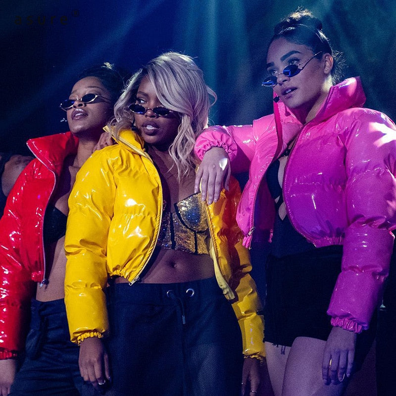 Drei Frauen in glänzenden, bunten Daunenjacken auf der Bühne, modische Sonnenbrillen, Nachtclub.