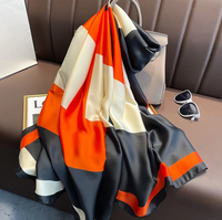 Seidenschal mit geometrischem Muster in Orange, Schwarz und Weiß auf Ledersofa drapiert.