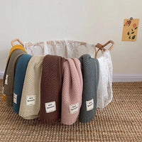 Mehrfarbige Babydecken aus Baumwolle in einem weißen Korb auf einem Teppich.