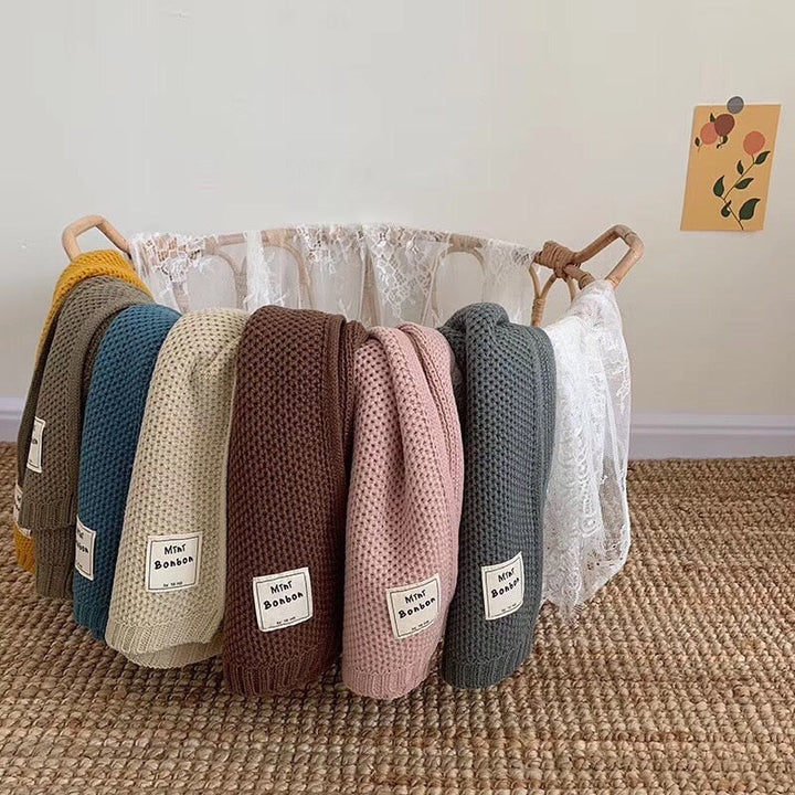 Mehrfarbige Babydecken aus Baumwolle in einem weißen Korb auf einem Teppich.