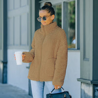 Frau in brauner Fleecejacke mit Kaffeebecher und Handtasche, draußen stehend.