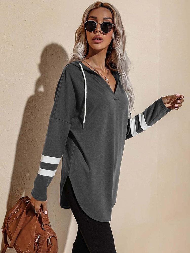 Frau in grauem Hoodie mit weißen Streifen, Sonnenbrille, braune Tasche, lässige Mode.