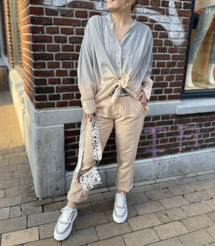 Frau in beiger Hose und grauem Hemd, weiße Sneaker, Leoparden-Tasche, Straßenhintergrund.