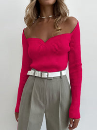 Frau in pinkem, schulterfreiem Strickpullover, graue Hose, weißer Gürtel, modisch, elegant.