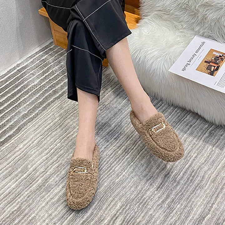 Damen Hausschuhe, beige, Plüsch, mit goldener Schnalle, gemütlich, auf gestreiftem Teppich.