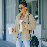 Frau in beiger Teddyjacke, Sonnenbrille, Jeans, mit Kaffeebecher und schwarzer Tasche.