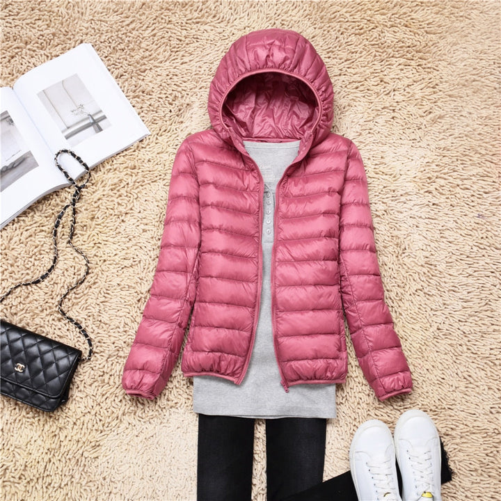Rosa Daunenjacke mit Kapuze, Damenmode, Winterjacke, warm, stilvoll, auf Teppich liegend.