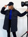 Frau in schwarzer Steppjacke, blaue Mütze, blaue Bluse, Fotostudio-Hintergrund.