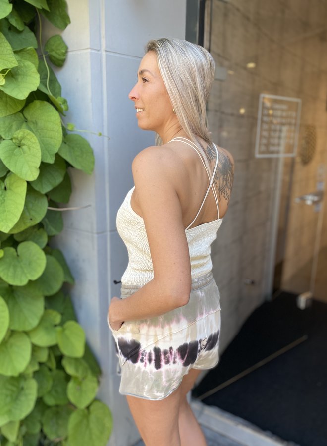 Frau in weißem Top und Batik-Shorts vor grüner Wand, Sommermode, lässiger Stil.