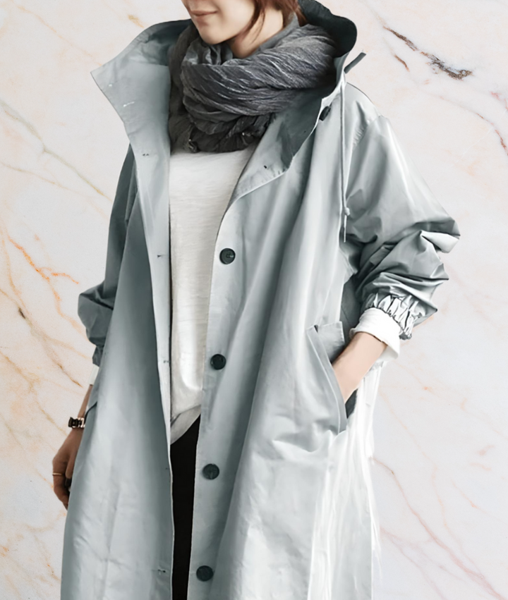 Frau in grauem Regenmantel mit Schal vor Marmorhintergrund.