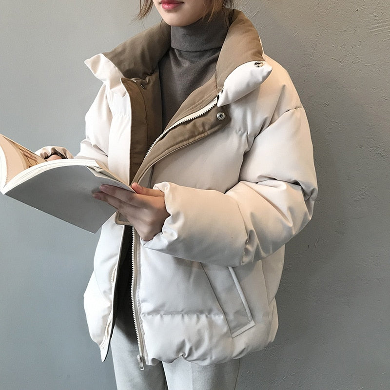 Frau in weißer Daunenjacke, hält ein Buch, Wintermode, warme Oberbekleidung, stilvoll.